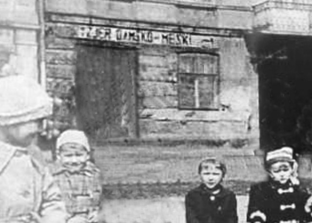 Foto archiwalne, za dziećmi w piaskownicy widać fragmenty zakładu fryzjerskiego Czesława Szmagaja