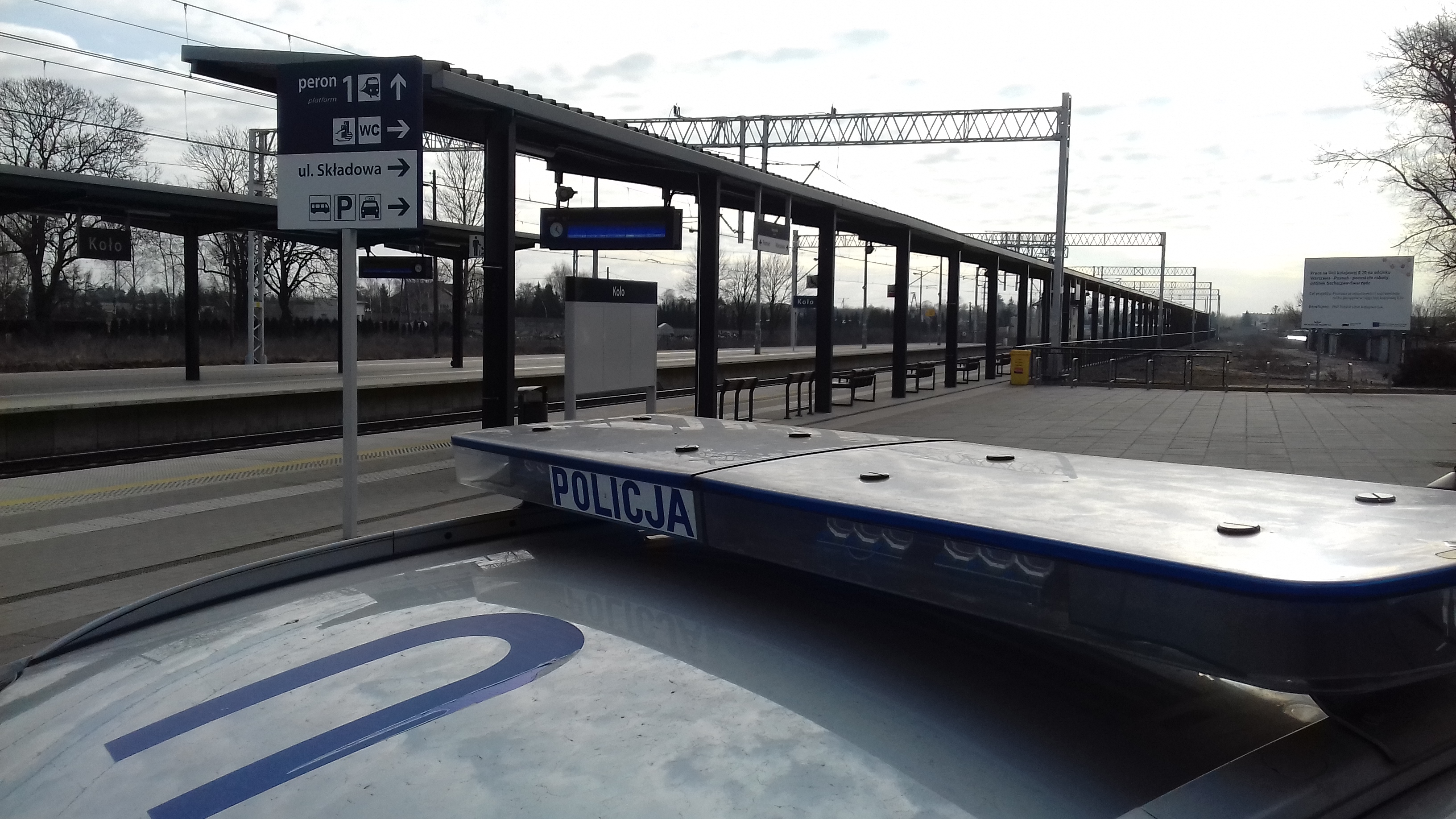 Zdjęcie przedstawia dach radiowozu policyjnego stojącego na dworcu kolejowym w Kole, w tle perony.