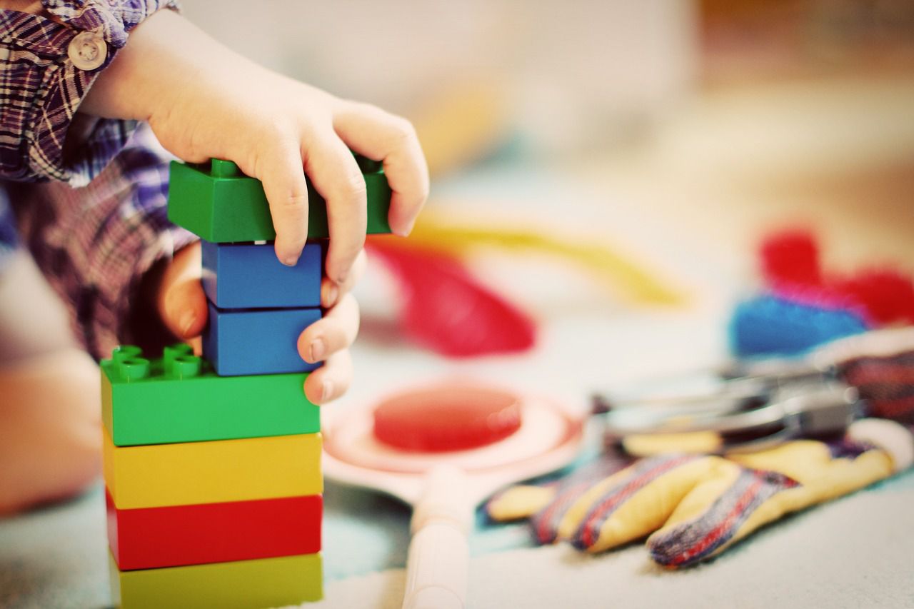 Zdjęcie przedstawia dziecko bawiące się klockami, w tle zamazane kolorowe zabawki