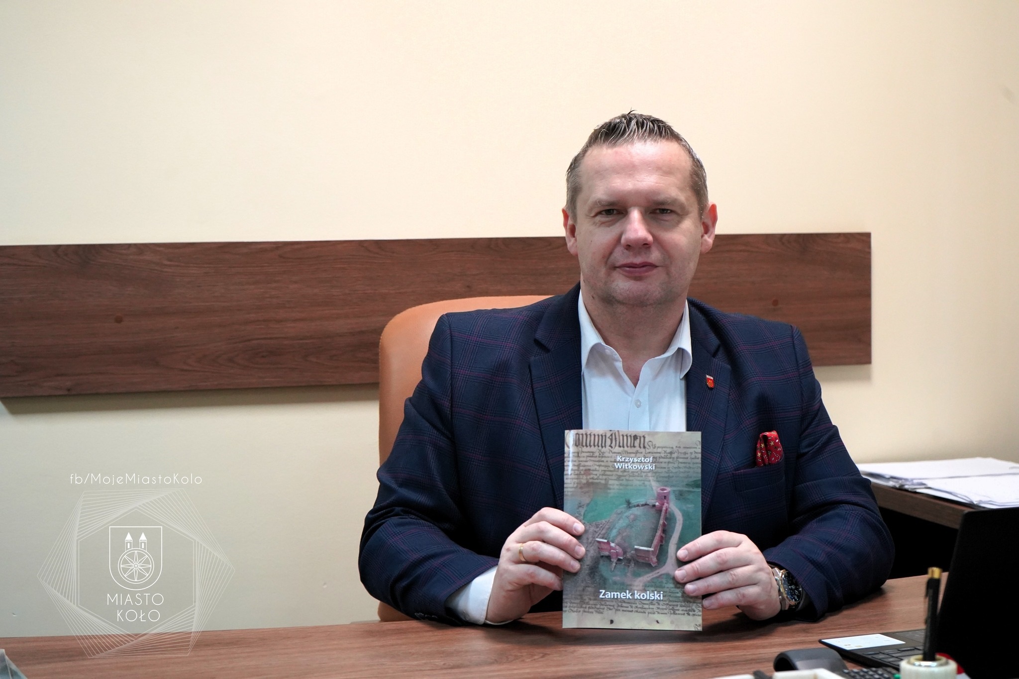 Burmistrz Miasta Koła Krzysztof Witkowski trzyma w dłoniach publikację o zamku królewskim w Kole