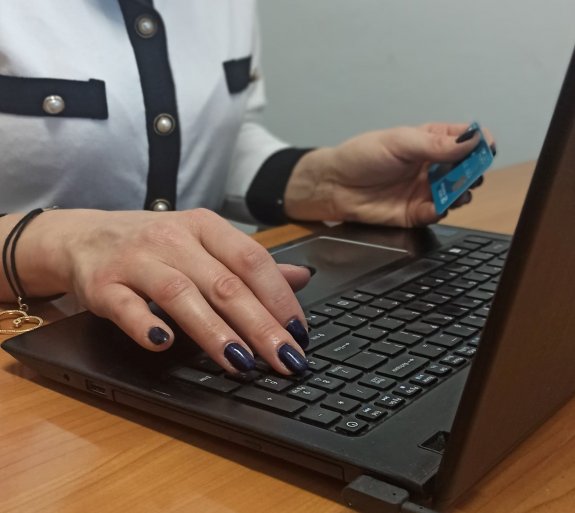 Zdjęcie przedstawia osobę przy laptopie z kartą bankową w dłoni.