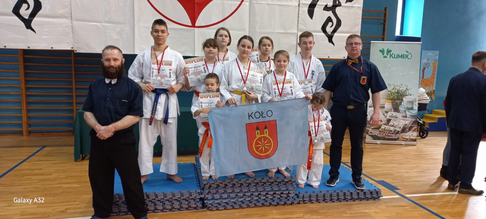 Kolscy karatecy Kolski Klub Kyokushin Karate stoją z dyplomami i flagą miasta Koła