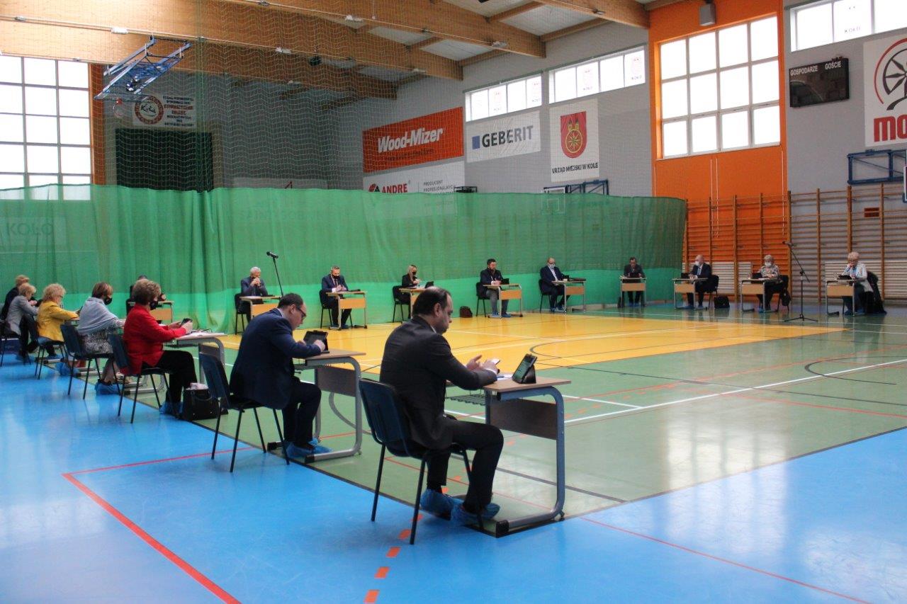 Zdjęcie przedstawia obradujących radnych wraz z władzami miasta Koła w hali sportowej MOSiR w Kole.