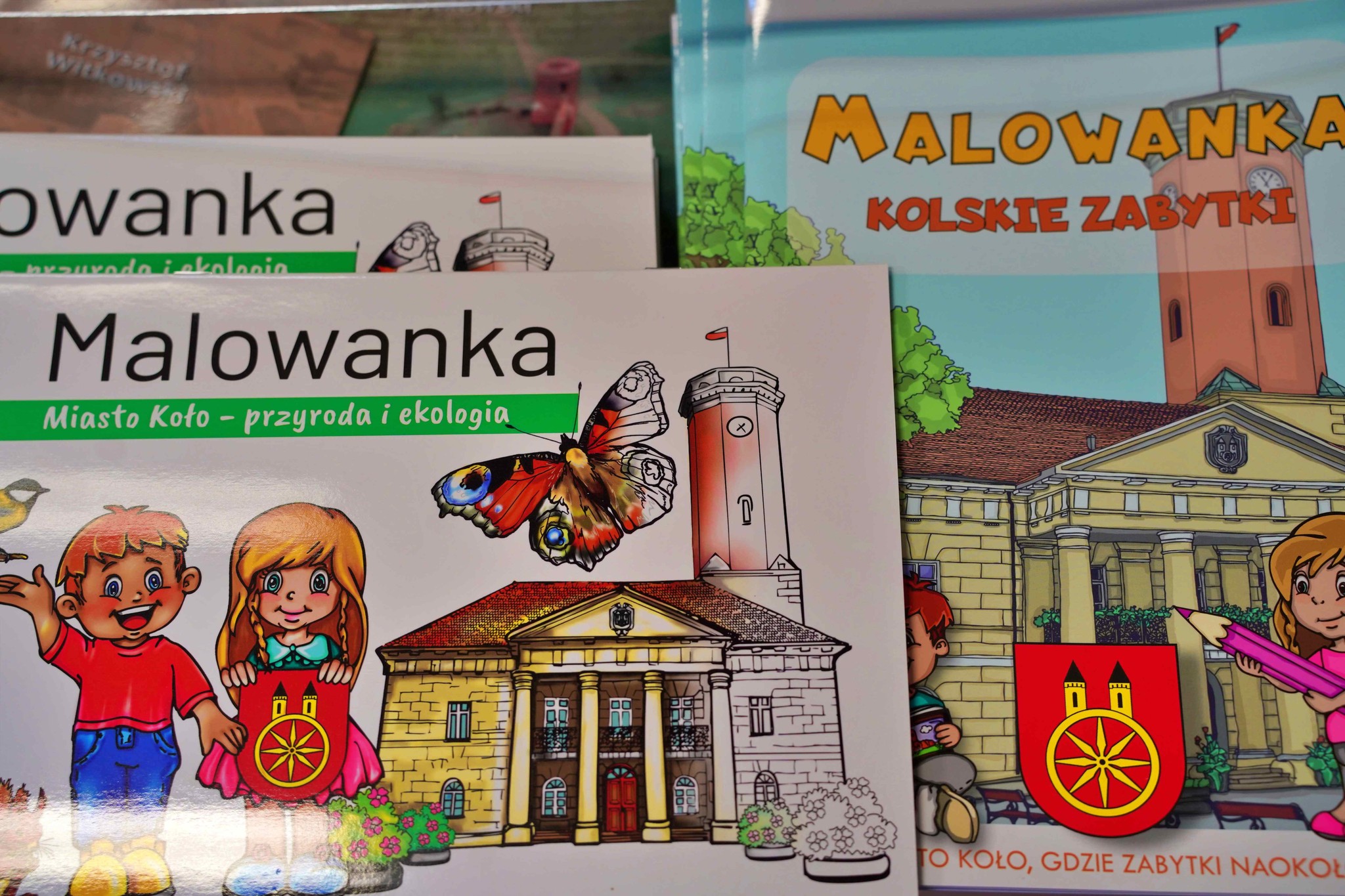 Zdjęcie przedstawia kolorowanki edukacyjne w języku polskim. Na okładkach widnieje napis „Malowanka” oraz tytuły: „Miasto Koło – przyroda i ekologia” i „Kolskie zabytki”. Ilustracje przedstawiają budynki, takie jak ratusz, dzieci, a także herb Koła