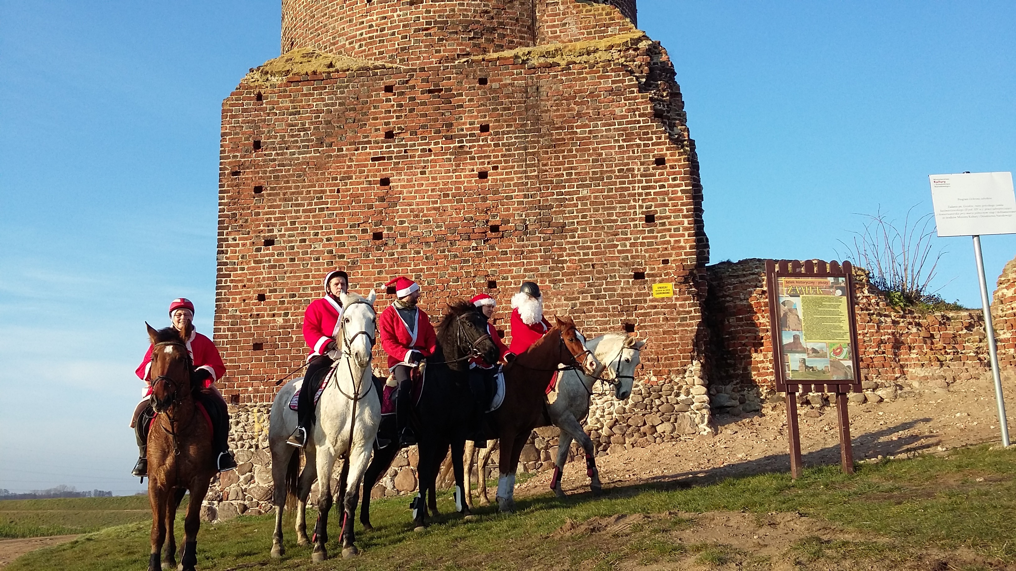 Zdjęcie przedstawia jeźdźców na koniach przed ruinami zamku w Kole przebranych za Mikołaje.