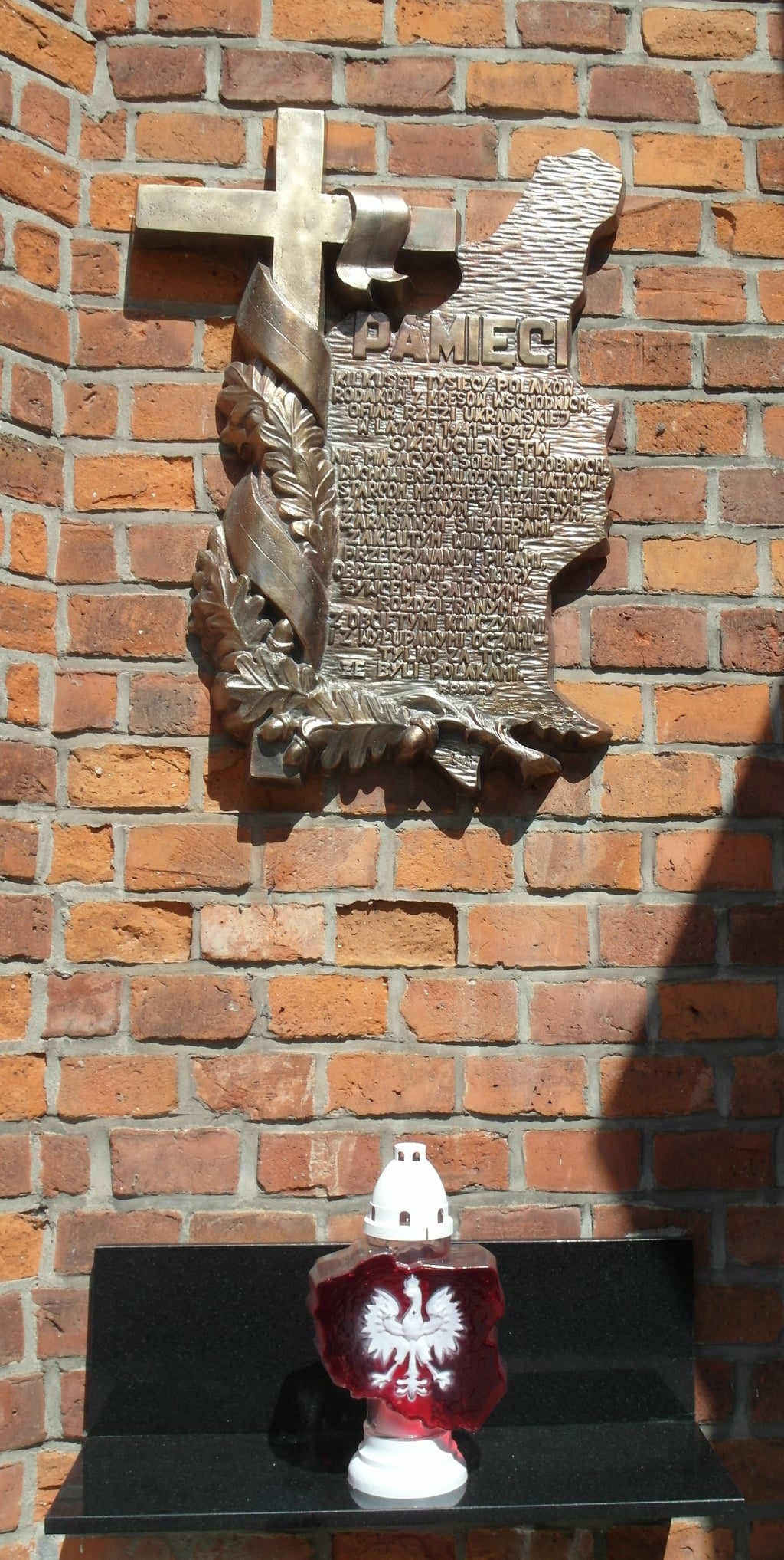 Znicz Pamięci pod tablicą upamiętniającą ofiary na murach kaplicy cmentarza parafialnego w Kole