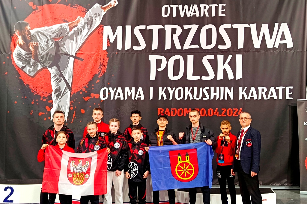 Zawodnicy Kolskiego Klubu Sportów Walki z pucharami, flagą miejską i dyplomami wraz z opiekunem.