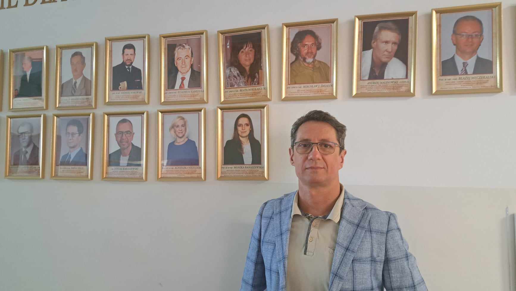 Zdjęcie przedstawia mężczyznę w okularach, w tle zdjęcia w ramkach na ścianie LO w Kole