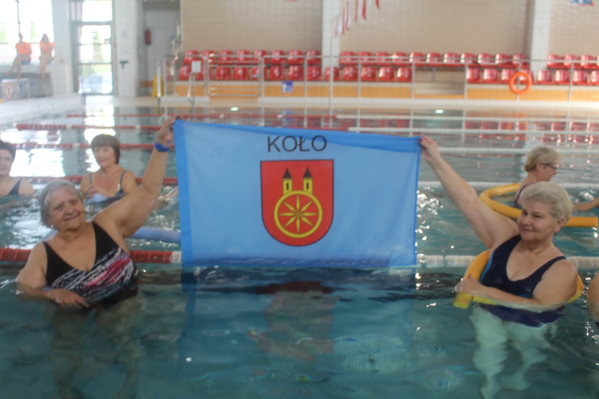 Kolscy seniorzy na pływalni z flagą miasta Koła.